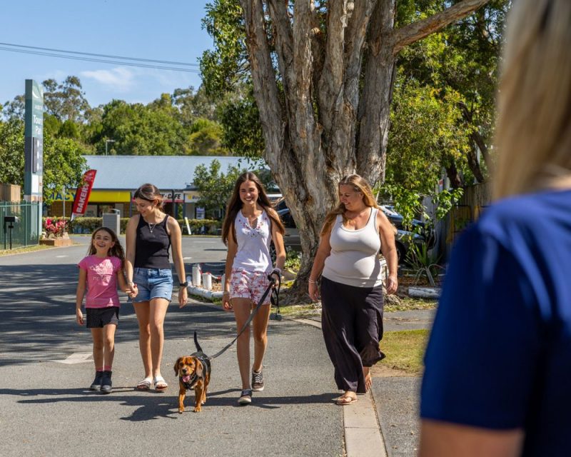 Two adults and two children walking a small brown dog on a lead along a quiet street at Jacobs Well Tourist Park on the northern Gold Coast.