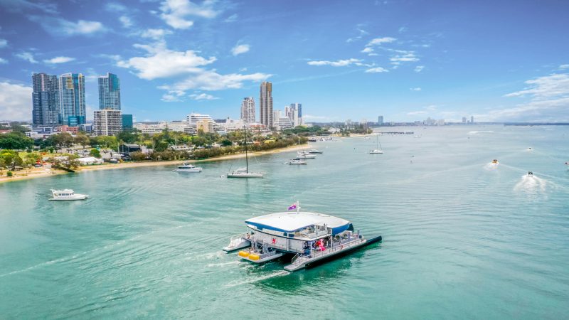 A scenic view of boats cruising on the Gold Coast Broadwater with the city skyline in the background under a blue sky.